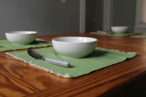 Green placemats with white bowls and grey handled spoons. Hygge handwoven acrylic placemats
