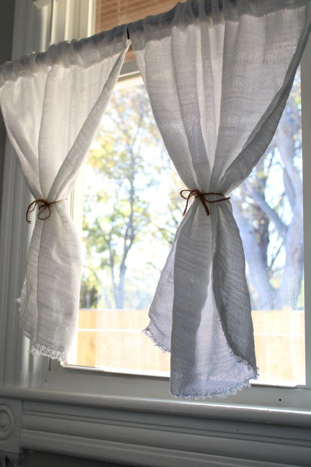 White curtains tied back with twine in sunny window. Hygge handwoven bistro curtains.